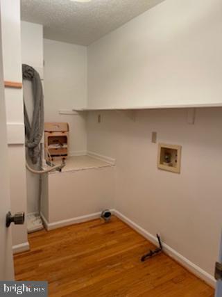 clothes washing area featuring a textured ceiling, laundry area, washer hookup, wood finished floors, and baseboards