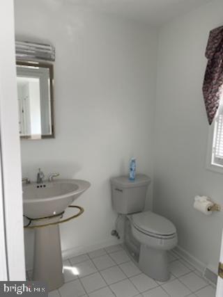 half bathroom with a sink, tile patterned flooring, toilet, and baseboards