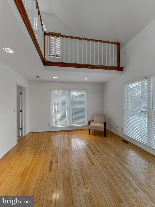 unfurnished room with visible vents, a towering ceiling, and light wood-style floors