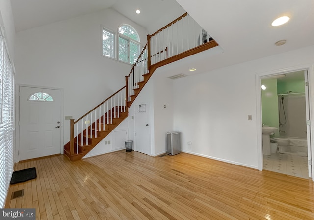 unfurnished living room with high vaulted ceiling, light wood-style flooring, stairs, and visible vents