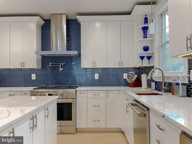 kitchen with stainless steel appliances, decorative backsplash, white cabinetry, a sink, and wall chimney exhaust hood