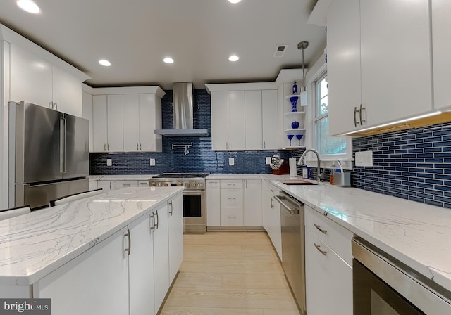 kitchen featuring stainless steel appliances, white cabinets, a sink, and wall chimney range hood