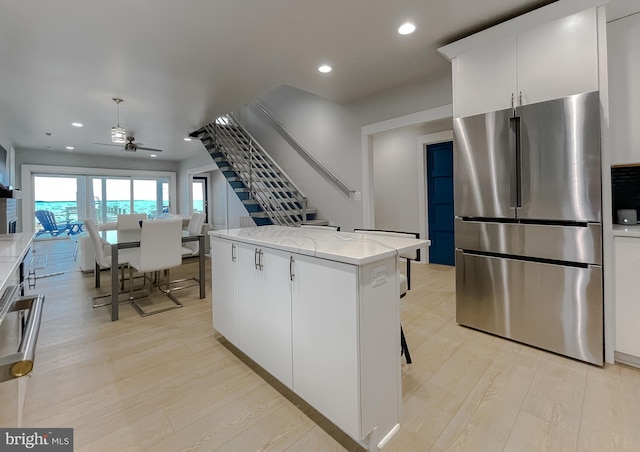 kitchen with light wood-style flooring, recessed lighting, a kitchen island, freestanding refrigerator, and light stone countertops