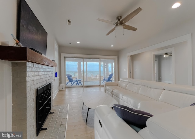 living room with light wood-type flooring, recessed lighting, a brick fireplace, and a ceiling fan