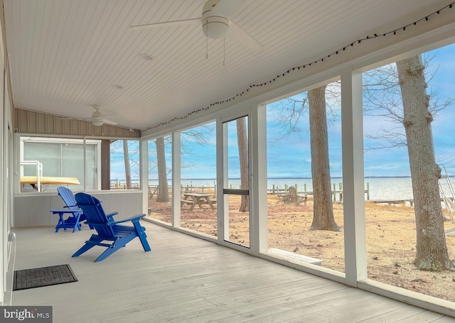 unfurnished sunroom featuring a water view, a beach view, and a ceiling fan