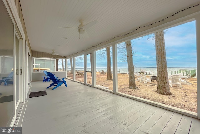 unfurnished sunroom featuring a ceiling fan, a beach view, a wealth of natural light, and a water view