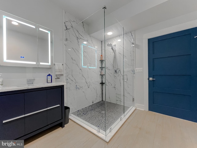 bathroom featuring wood finished floors, a marble finish shower, and vanity