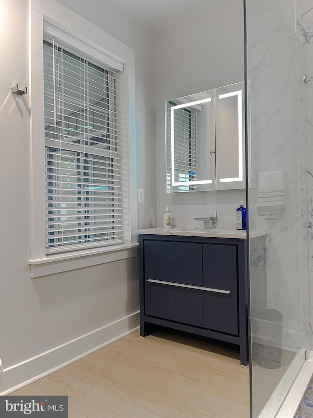 bathroom with a marble finish shower, baseboards, wood finished floors, and vanity