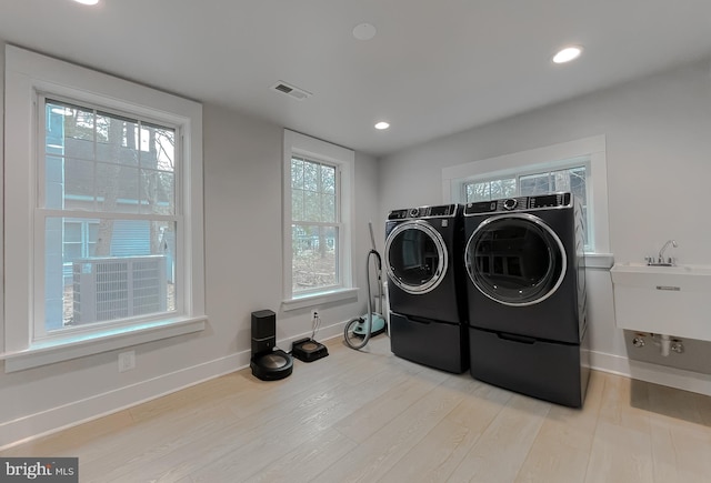 laundry area featuring washing machine and dryer, light wood-style flooring, laundry area, a sink, and visible vents