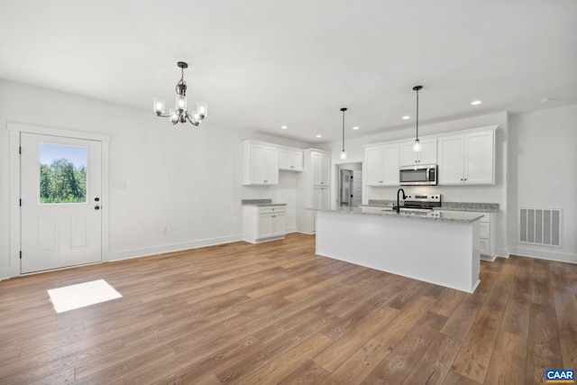 kitchen with stainless steel appliances, a center island with sink, visible vents, and white cabinets