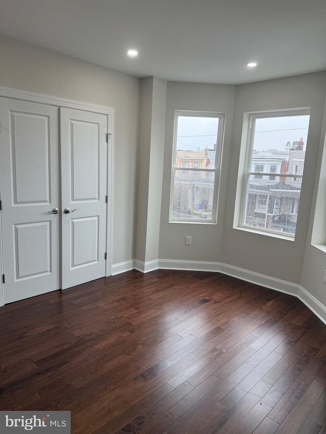 empty room with dark wood-style flooring, recessed lighting, and baseboards