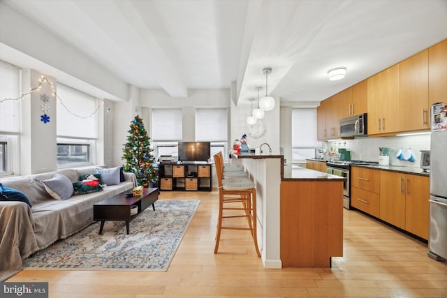 kitchen featuring a breakfast bar area, open floor plan, hanging light fixtures, appliances with stainless steel finishes, and dark countertops