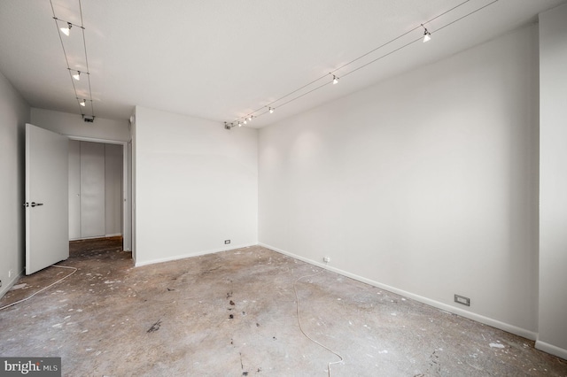 empty room featuring track lighting, baseboards, and unfinished concrete flooring