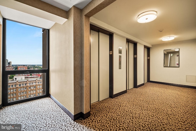 hallway featuring light carpet, baseboards, elevator, a wall of windows, and a city view