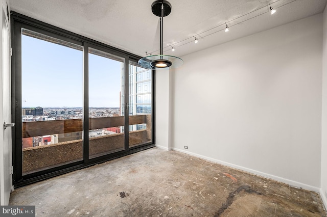 unfurnished dining area featuring rail lighting, unfinished concrete flooring, and baseboards