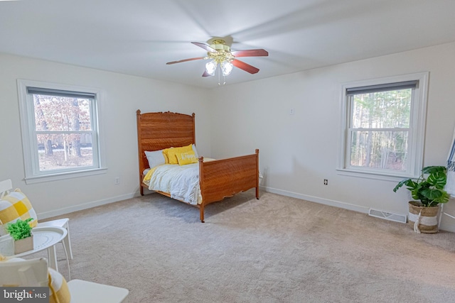 carpeted bedroom featuring visible vents, multiple windows, baseboards, and ceiling fan