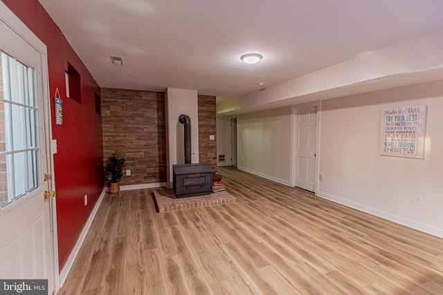 interior space featuring light wood finished floors, a wood stove, baseboards, and an accent wall