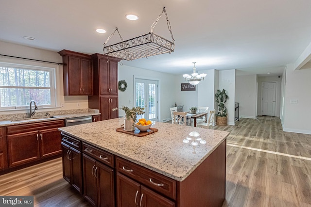 kitchen with a chandelier, light wood-style flooring, stainless steel dishwasher, and a sink