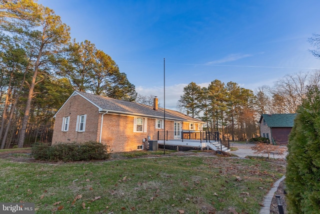 back of property featuring a wooden deck, a yard, central AC, a chimney, and brick siding