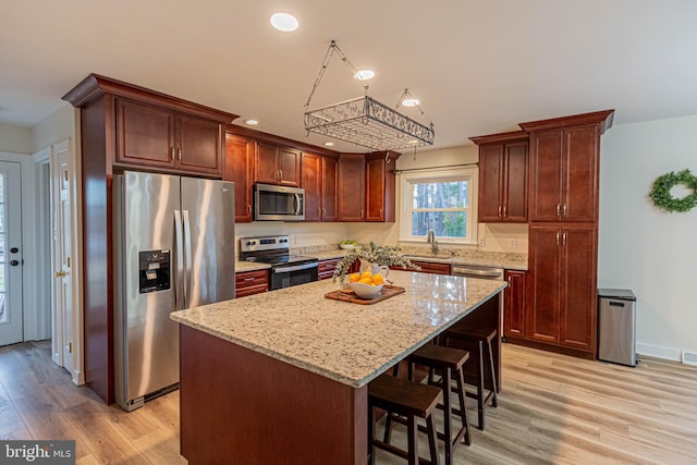 kitchen with a kitchen bar, a kitchen island, light wood-style floors, appliances with stainless steel finishes, and light stone countertops