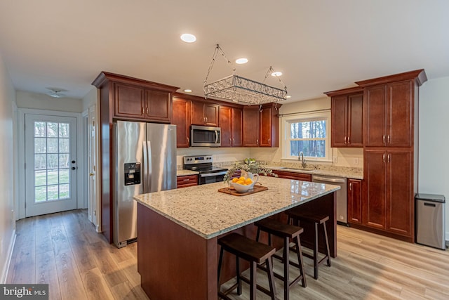 kitchen featuring light stone countertops, light wood-style floors, appliances with stainless steel finishes, and a sink