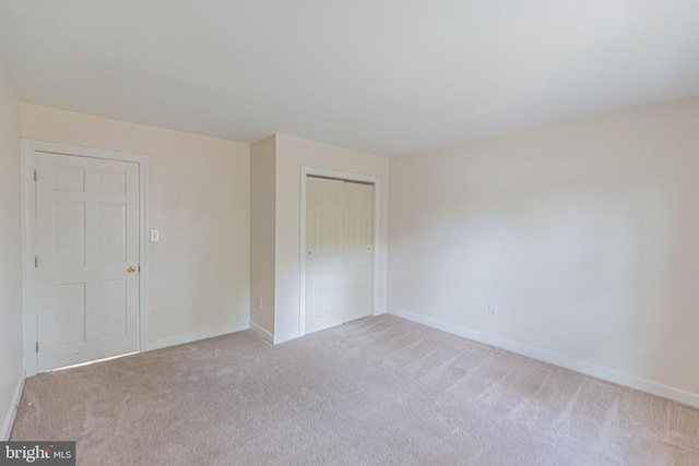 unfurnished bedroom with a closet, light carpet, and baseboards