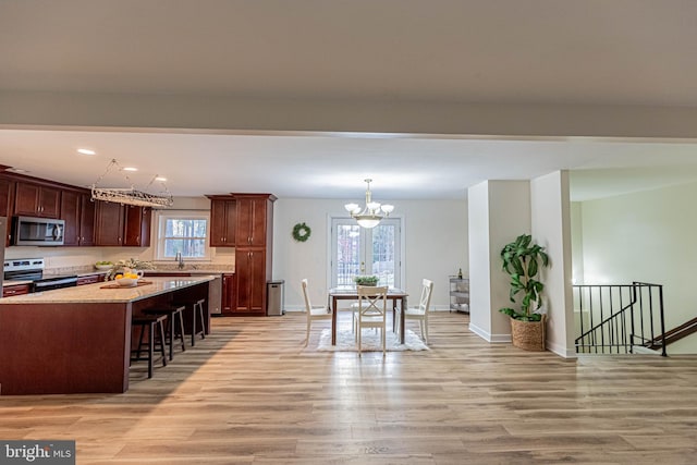 kitchen featuring light wood-type flooring, stainless steel appliances, a kitchen bar, and a chandelier