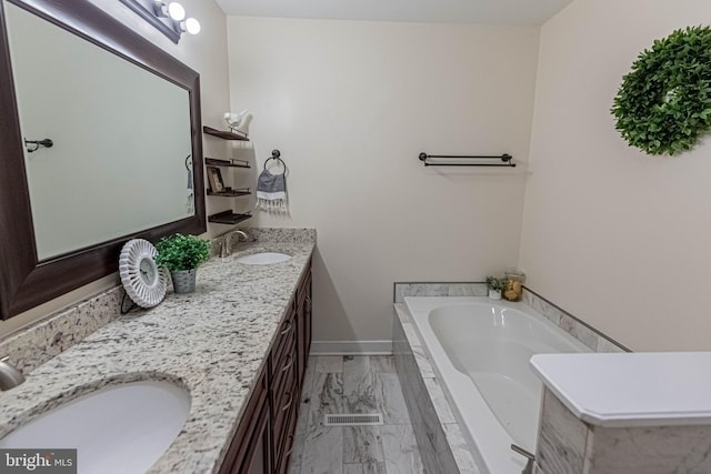 full bath with double vanity, marble finish floor, a garden tub, and a sink