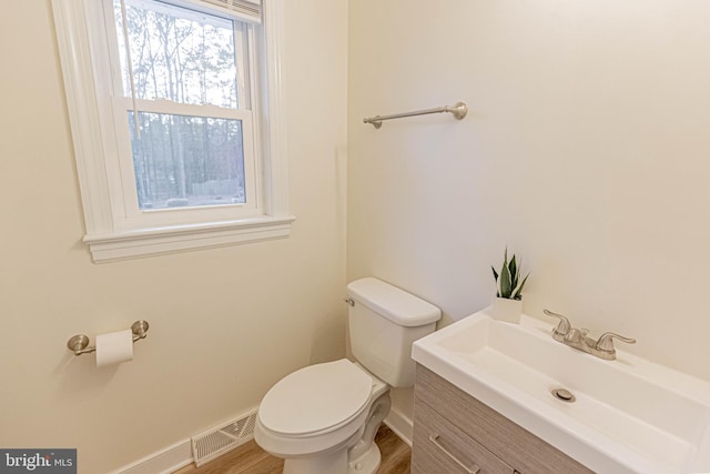 half bathroom featuring visible vents, baseboards, toilet, wood finished floors, and vanity