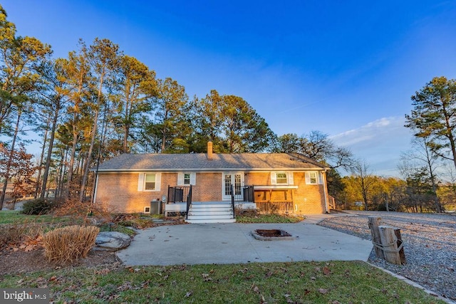 view of front of property featuring brick siding, a fire pit, french doors, and a chimney