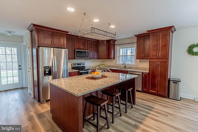 kitchen with a sink, a kitchen island, light wood-style floors, appliances with stainless steel finishes, and light stone countertops