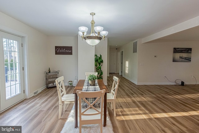 dining space featuring an inviting chandelier, baseboards, visible vents, and light wood finished floors