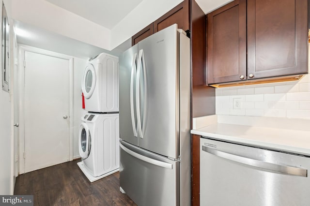 kitchen featuring dark wood-style flooring, light countertops, appliances with stainless steel finishes, tasteful backsplash, and stacked washer and clothes dryer