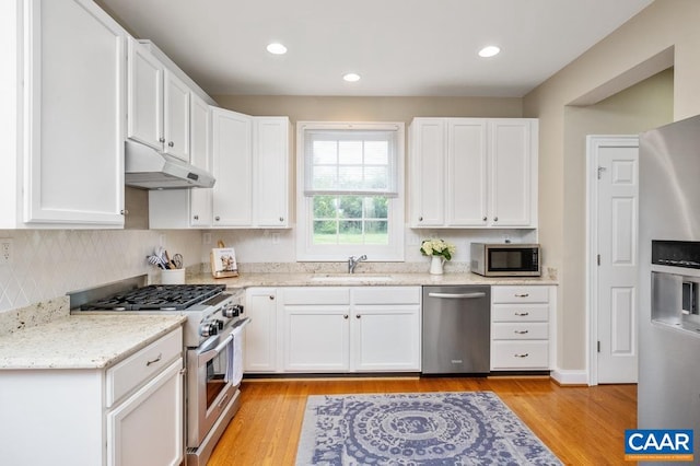 kitchen with appliances with stainless steel finishes, white cabinets, a sink, light stone countertops, and under cabinet range hood