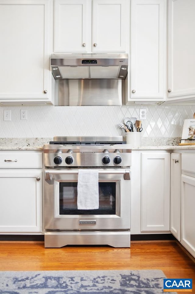 kitchen featuring under cabinet range hood, light wood-style floors, white cabinets, light stone countertops, and stainless steel range