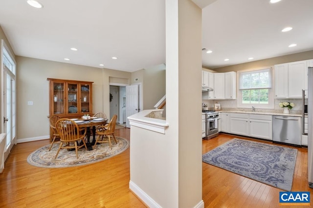 kitchen with stainless steel appliances, light countertops, white cabinets, light wood-type flooring, and under cabinet range hood