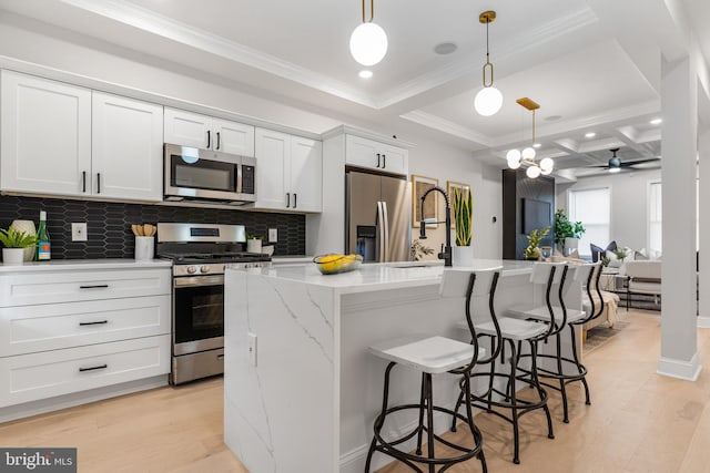 kitchen featuring stainless steel appliances, a kitchen island with sink, decorative light fixtures, and white cabinetry