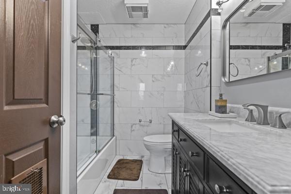 full bathroom with toilet, vanity, visible vents, marble finish floor, and combined bath / shower with glass door