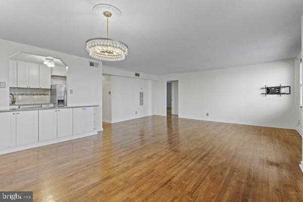 unfurnished living room featuring a chandelier, visible vents, light wood-style flooring, and baseboards