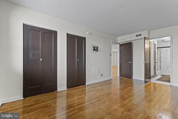 unfurnished bedroom featuring visible vents, two closets, baseboards, and wood finished floors