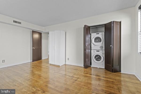 interior space with laundry area, visible vents, stacked washing maching and dryer, and wood finished floors