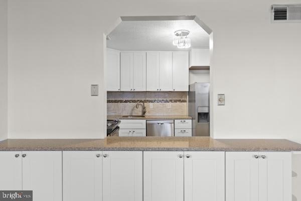 kitchen featuring visible vents, appliances with stainless steel finishes, white cabinets, a sink, and dark stone counters