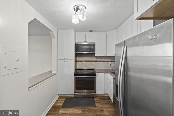 kitchen featuring pendant lighting, dark wood-style flooring, backsplash, appliances with stainless steel finishes, and white cabinets