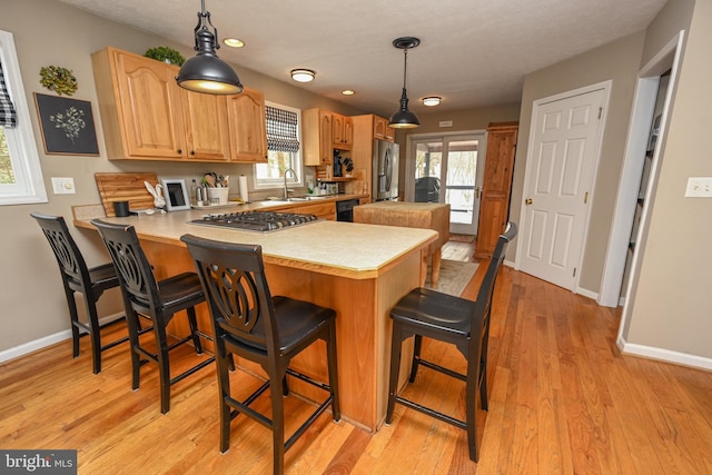 kitchen with a peninsula, hanging light fixtures, stainless steel appliances, light countertops, and a sink