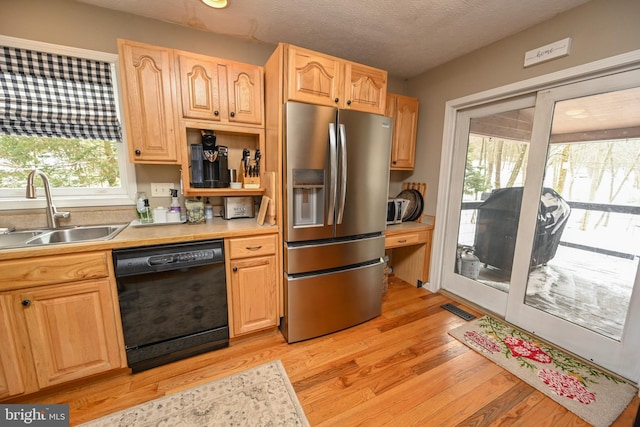 kitchen featuring a sink, visible vents, black dishwasher, light countertops, and stainless steel fridge