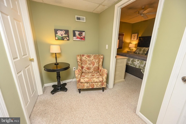 living area featuring a paneled ceiling, light colored carpet, visible vents, a ceiling fan, and baseboards