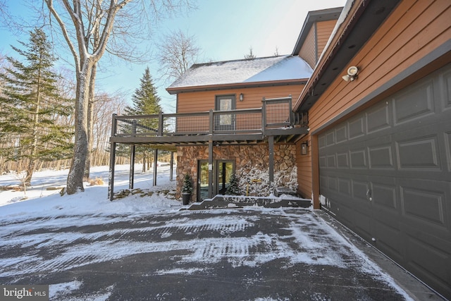 view of snowy exterior featuring a garage, stone siding, and driveway