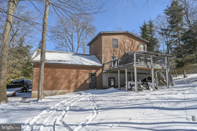 snow covered rear of property featuring a sunroom, stairs, and a deck