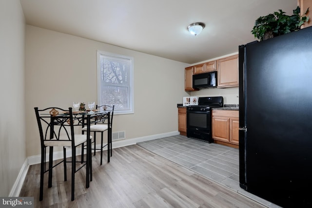 kitchen featuring visible vents, baseboards, light wood-style floors, black appliances, and dark countertops