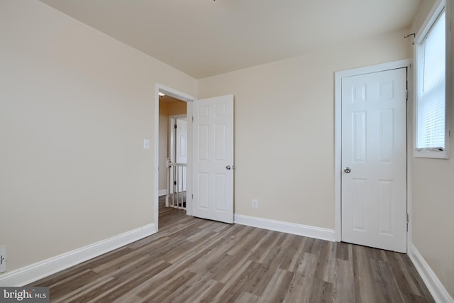 unfurnished bedroom featuring multiple windows, wood finished floors, and baseboards